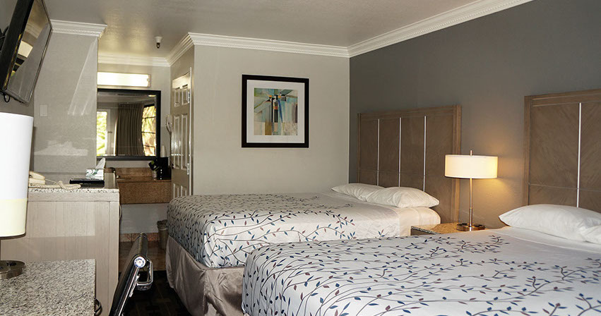 Showing 2 queen beds, writing desk, and entrance to restroom.