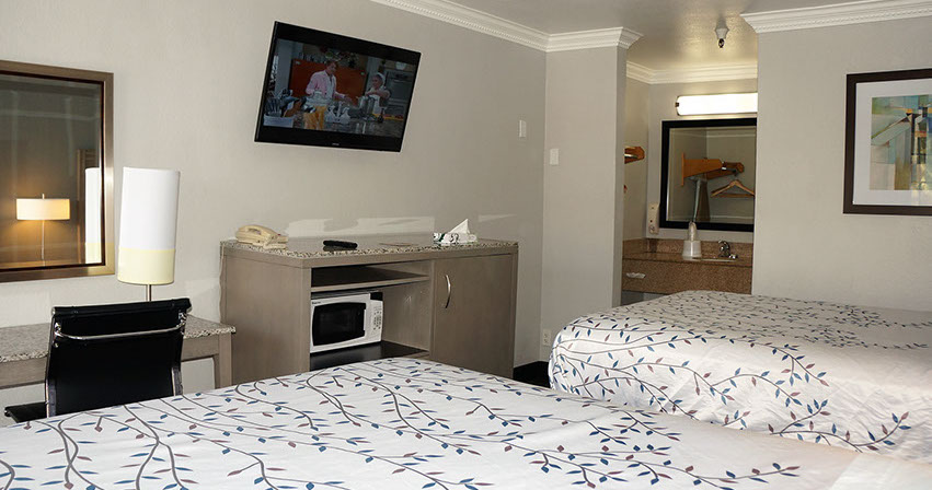 Showing 2 queen beds, writing desk, flat screen t.v. and entrance to restroom.