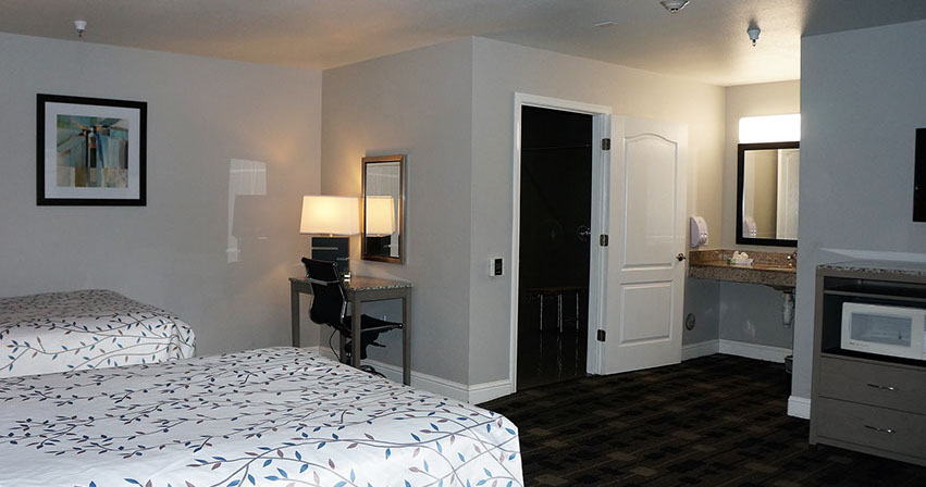 Photo showing beds, microwave, sink and bathroom area, writing desk and lamp.